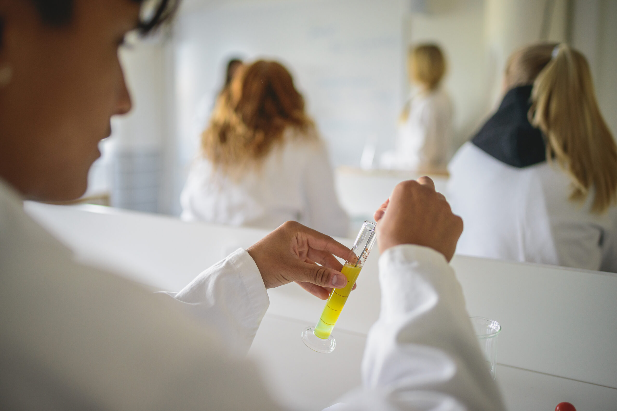 En elev i vit labbrock laborerar med en gul vätska i ett kemirör